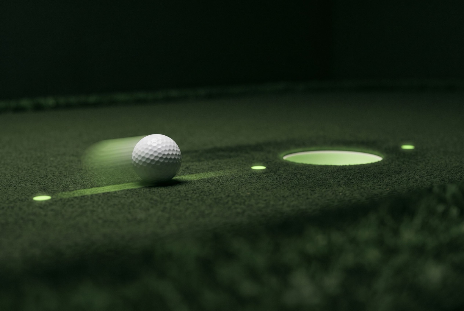 A golf ball rolling along a lit start line toward the cup on a practice green.